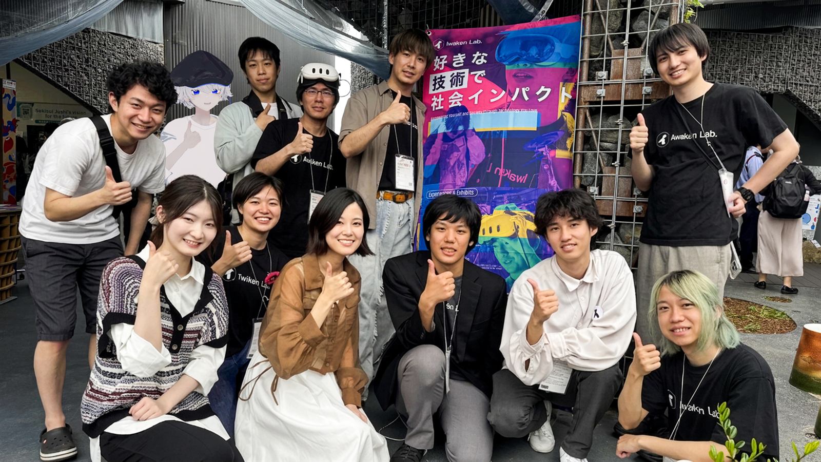 大阪・関西万博 XR Showcase の会場で、Iwaken Lab. のバナーを囲んでメンバーが笑顔で親指を立てている集合写真
