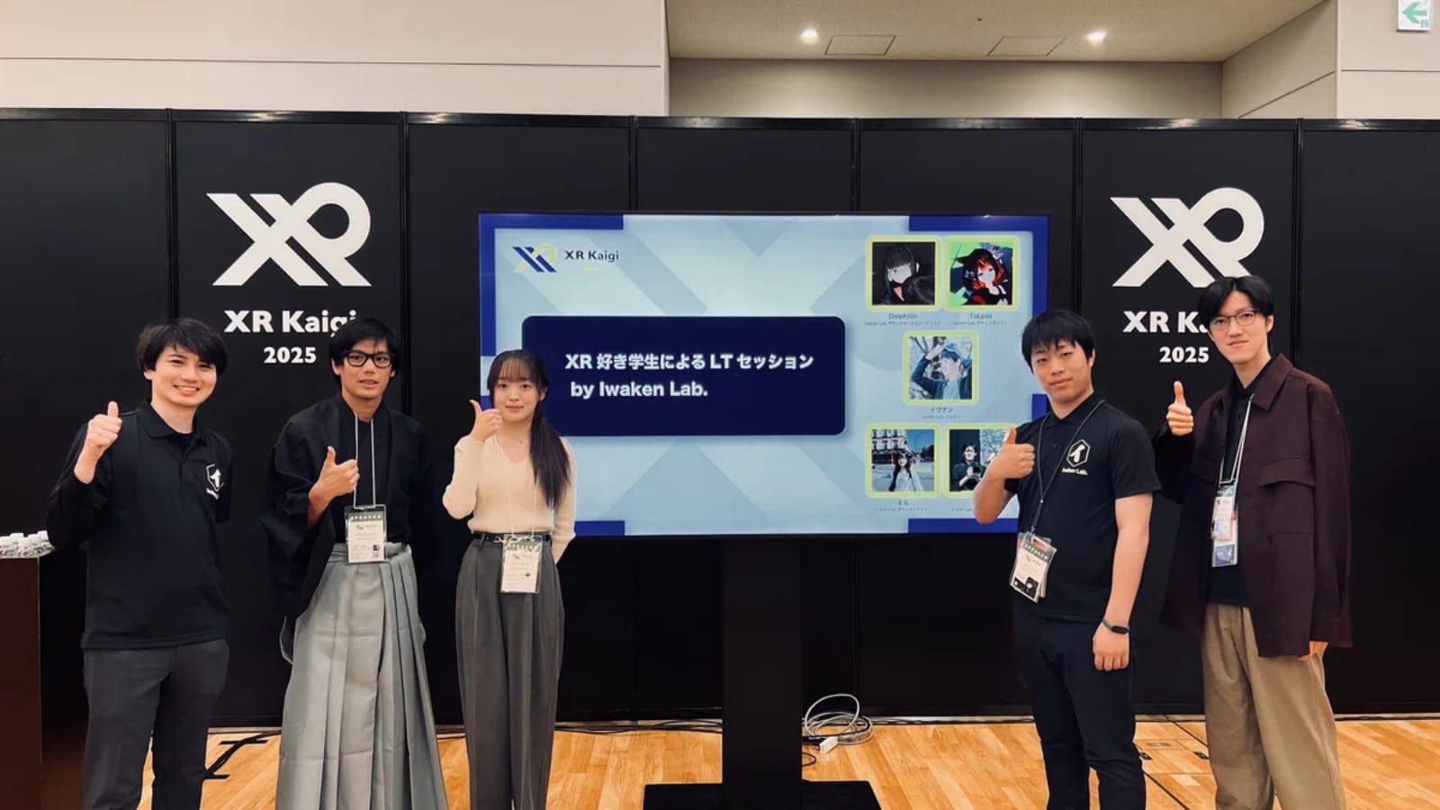 XR Kaigi 2025 の会場で、Iwaken Lab. メンバーが「XR 好き学生による LT セッション」のスクリーン前で親指を立てている様子